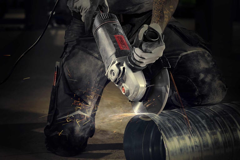 O persoană folosește un polizor unghiular pentru a tăia o țeavă metalică, producând scântei.