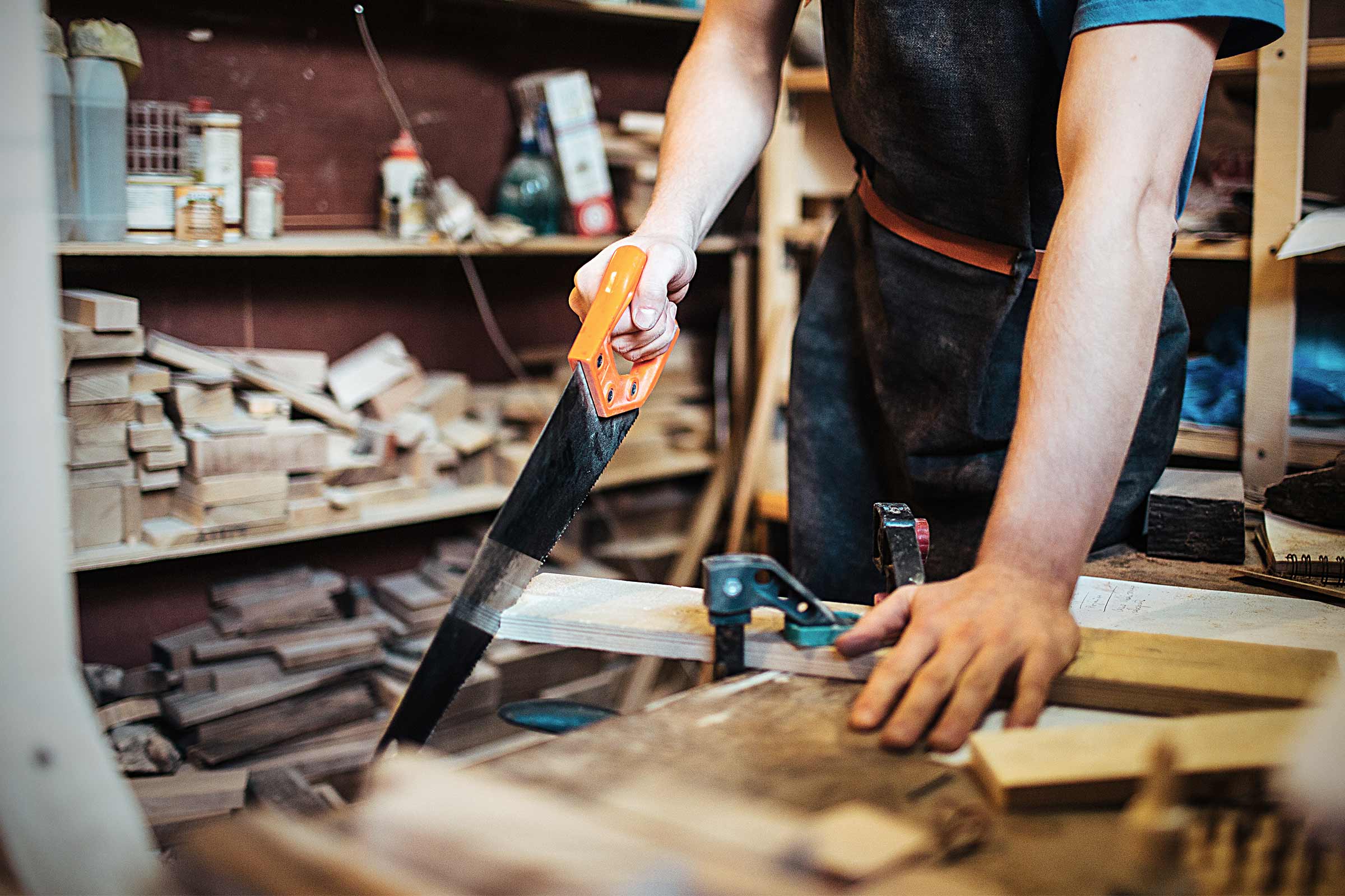 Artizan care taie lemn cu un fierăstrău manual într-un atelier.