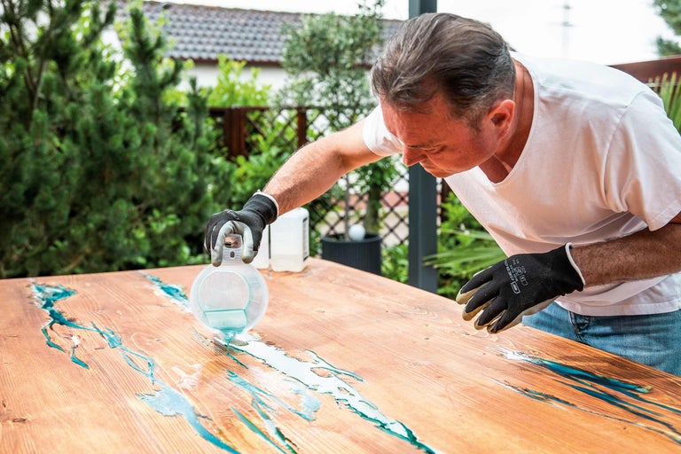 Bărbat turnând rășină epoxidică pe o masă din lemn în aer liber