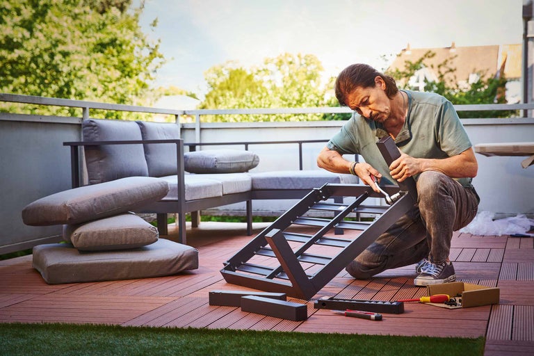 Femeie șlefuind o scândură de lemn afară cu un bloc de șlefuit pe un banc de lucru