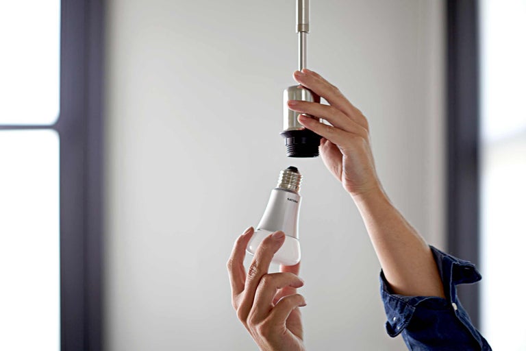 O persoană înșurubează un bec Philips într-un soclu.