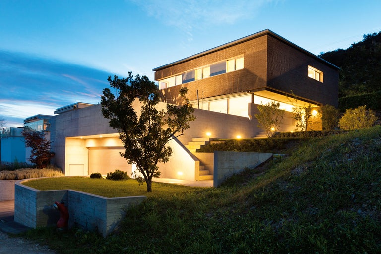 Casă modernă cu garaj, grădină și iluminat exterior la amurg
