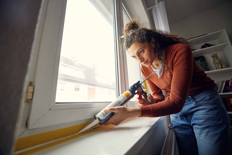 Femeie etanșează o fereastră cu etanșant