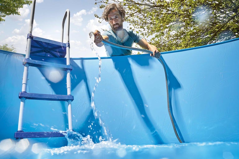 Bărbat umplând piscină supraterană cu un furtun de apă și o scară