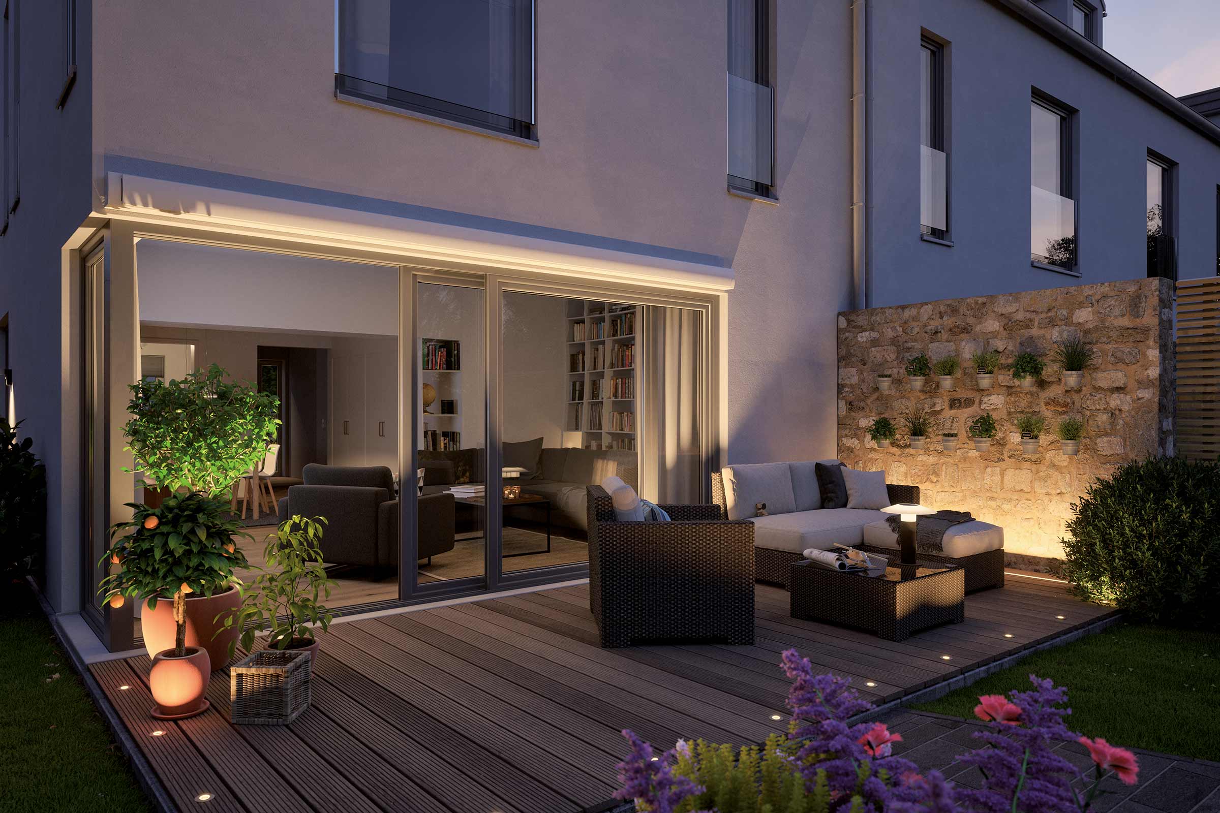 Terasa iluminată cu mobilier de grădină, plante și casă adiacentă