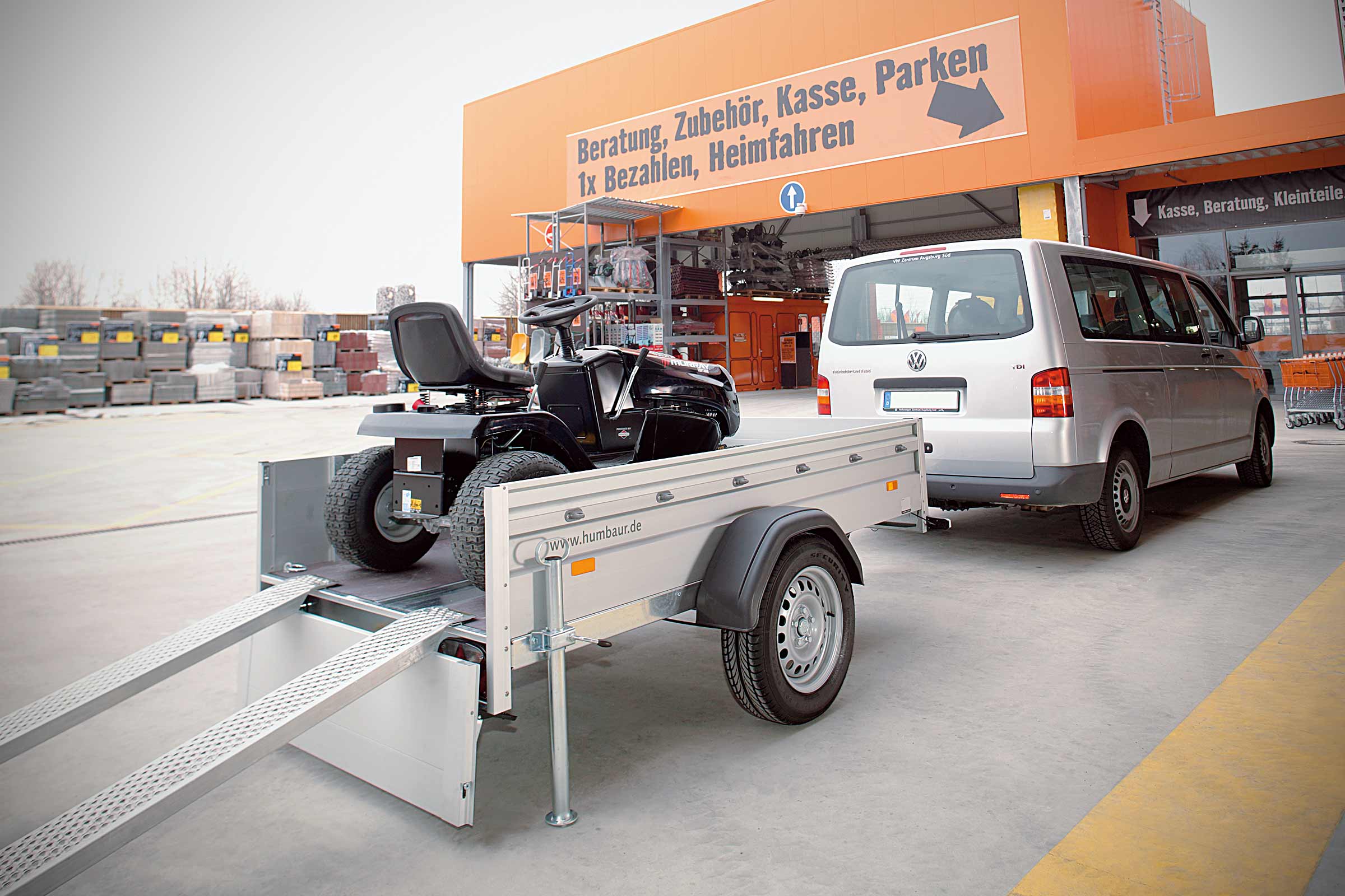 Un tractor de gazon pe o remorcă în fața unui magazin de bricolaj Hornbach.