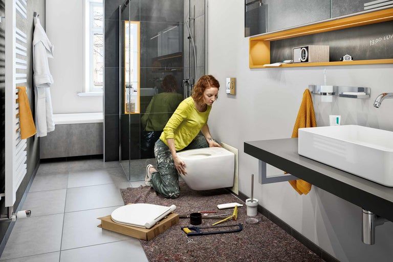 Femeie instalează o toaletă suspendată în baie.