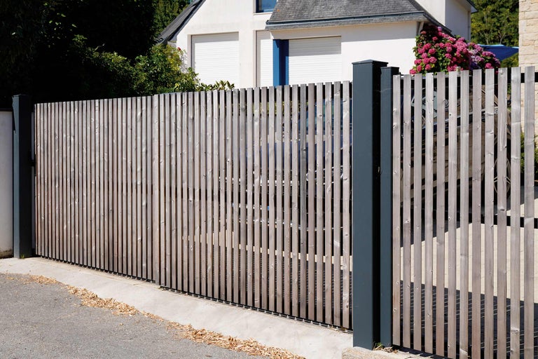 Gard din lemn cu șipci și stâlpi metalici în fața unei case