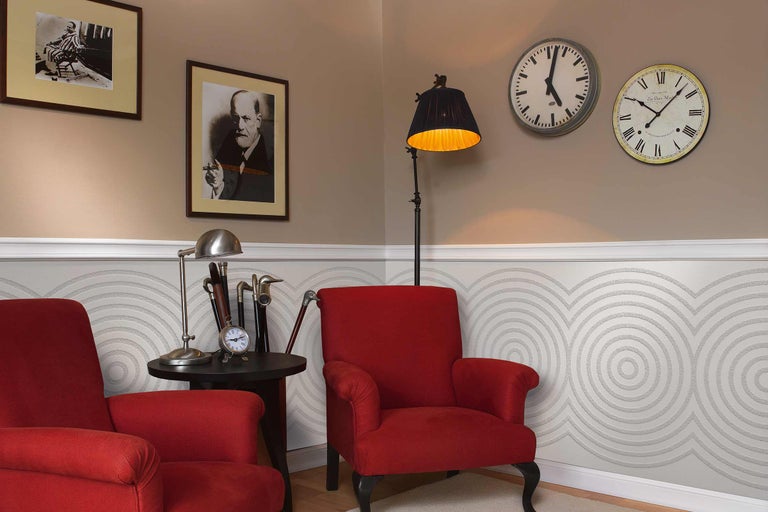 Imagine de interior cu două fotolii roșii, lampadar, lampă de masă, două ceasuri de perete și design decorativ pe perete