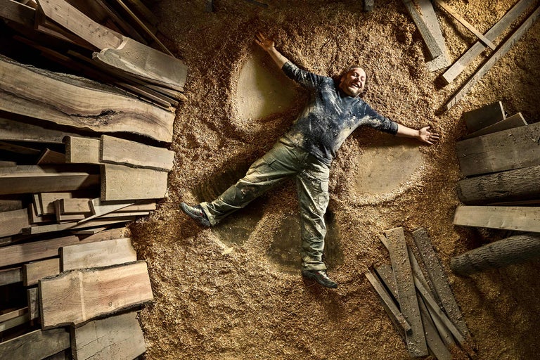 Bărbat întins cu brațele și picioarele întinse pe un morman de așchii de lemn printre scânduri de lemn