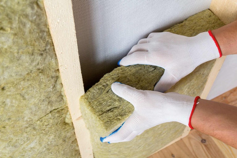 O persoană introduce vată minerală pentru izolare termică între rame de lemn.