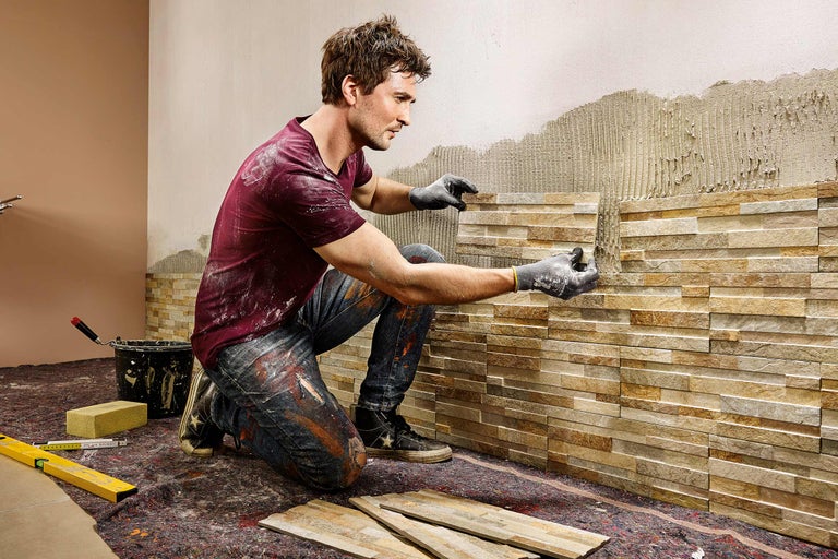 Artizan care montează placaj de perete din piatră naturală în interior