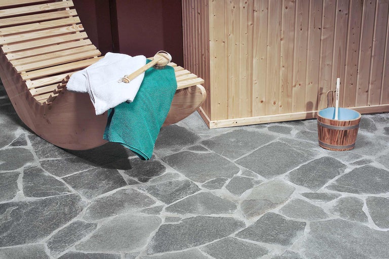 Interior de saună cu șezlong, prosoape, găleată pentru infuzie și podea de piatră