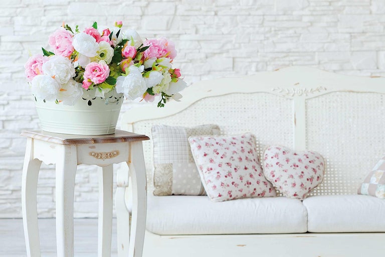 Scenă decorativă cu buchet de flori într-o găleată pe o măsuță laterală lângă o canapea cu perne