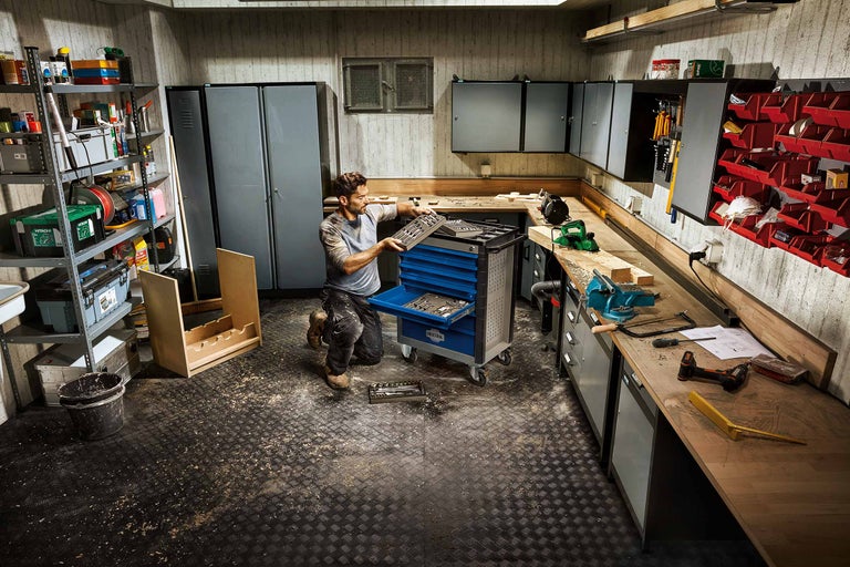 Atelier cu cărucior de scule, banc de lucru și rafturi pentru depozitarea sculelor.