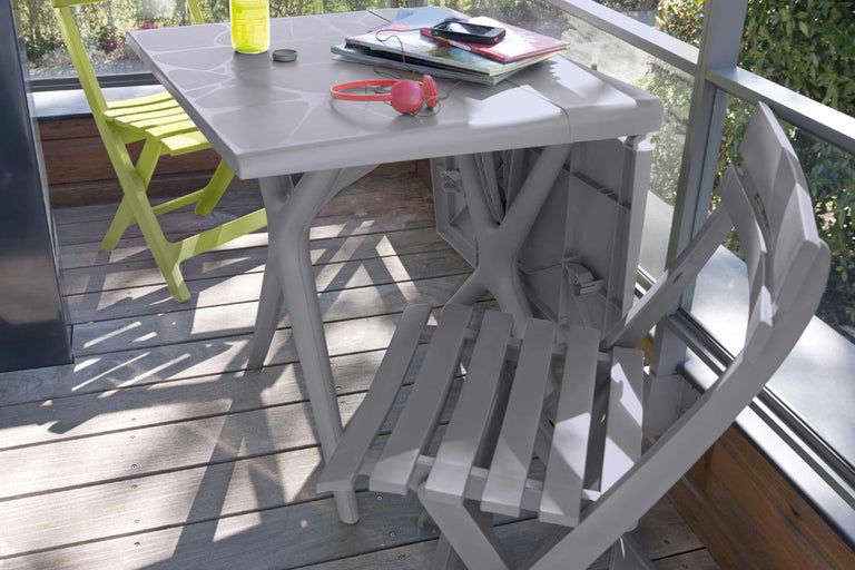 Scenă de grădină cu masă pliabilă gri, scaun pliabil verde și accesorii pe o terasă.