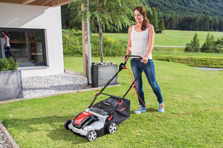 Femeie manevrând o mașină de tuns iarba în grădină.