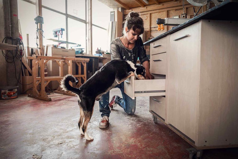 Femeie deschizând un sertar în atelier cu un câine