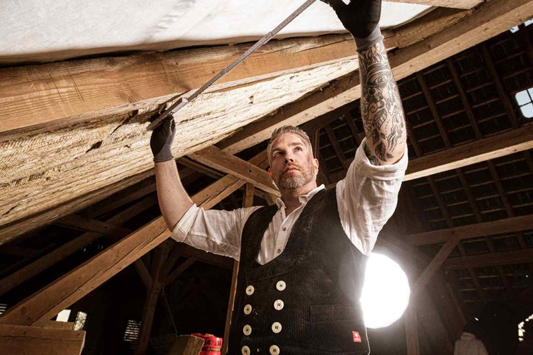 Meșter măsoară o grindă de acoperiș din lemn cu un metru pliant.