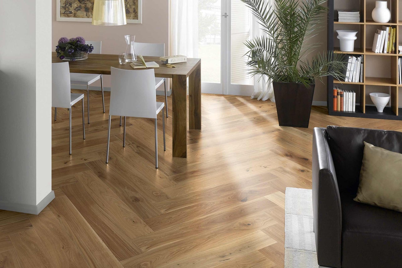 Scenă luminoasă de living cu parchet în model herringbone, masă de sufragerie, scaune și plantă de interior