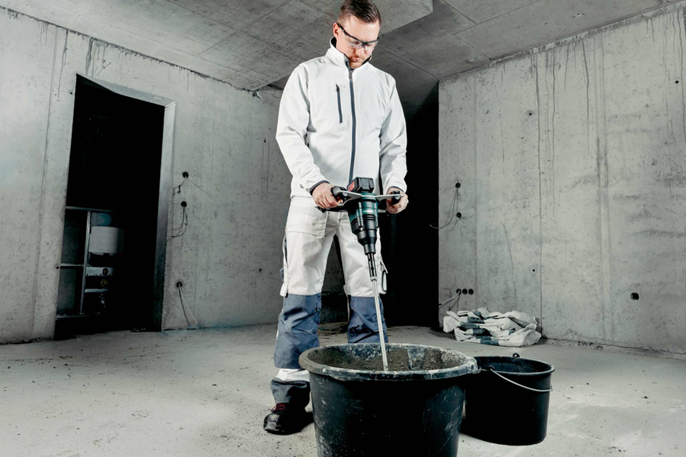 Meșter amestecând mortar cu un mixer într-o găleată pe un șantier.