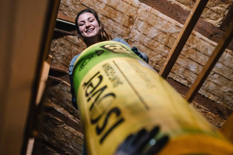 Femeie ținând o rolă de izolație în pod cu cadru din lemn și material izolant