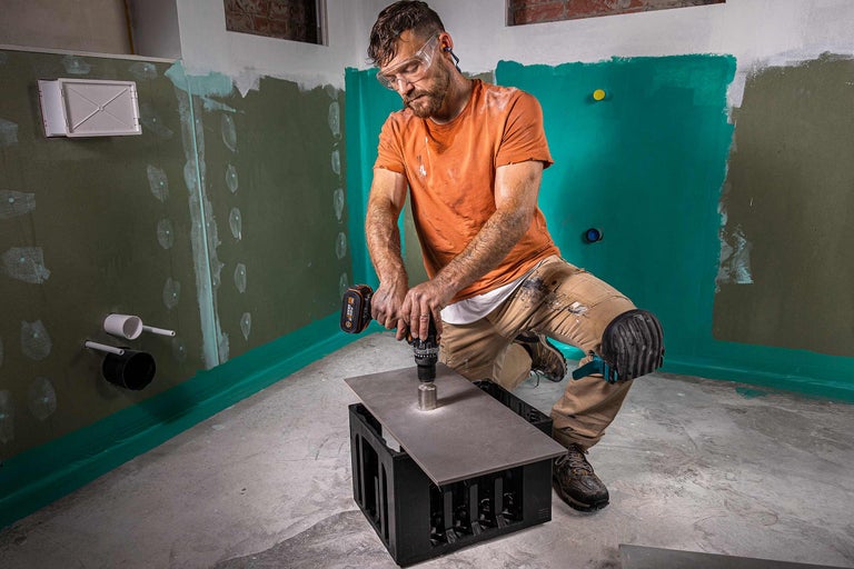 Un bărbat găurește o faianță cu o mașină de găurit într-o baie.