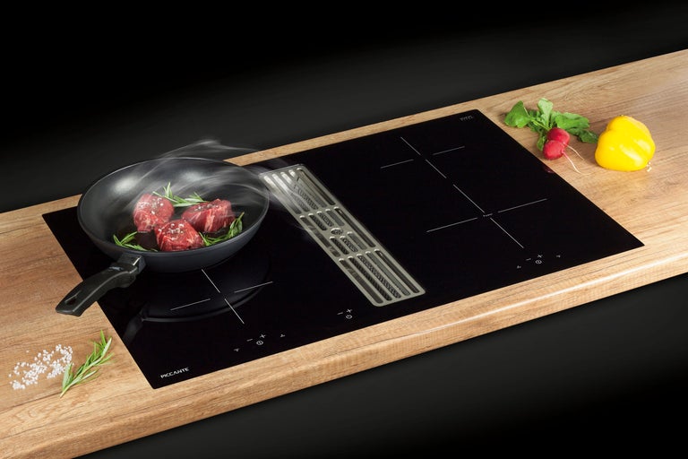 Plită cu inducție neagră cu hotă integrată lângă o tigaie pe un blat de lucru