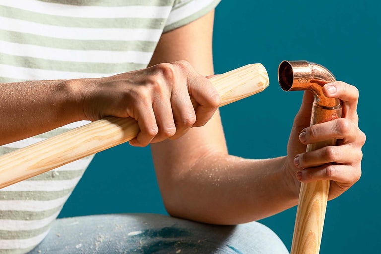 O persoană ține o țeavă de cupru și un băț de lemn.