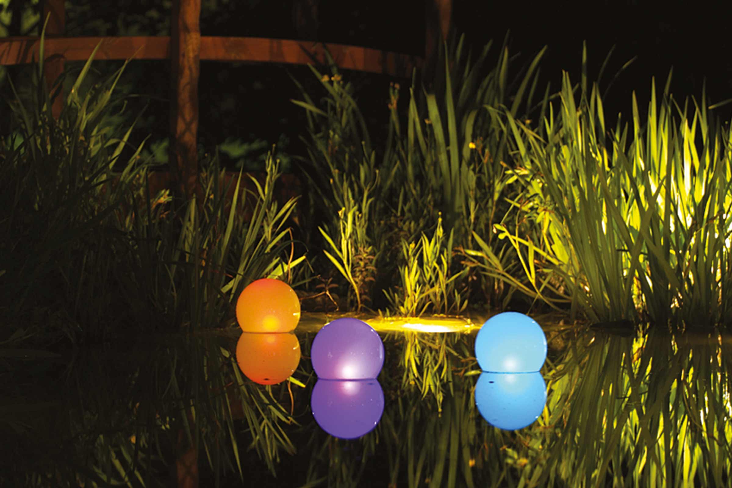 Trei bile plutitoare colorate iluminate pe un iaz printre plante.