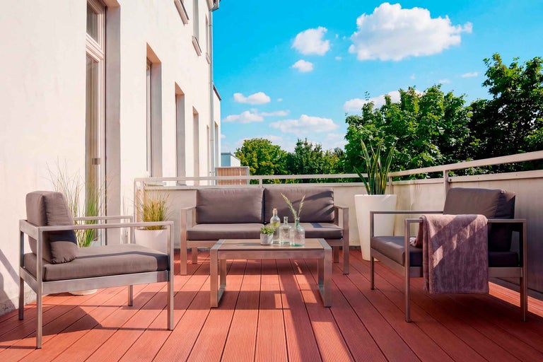 Set modern de grădină din metal cu perne gri pe o terasă cu deck WPC, compus din canapea, fotolii și masă.