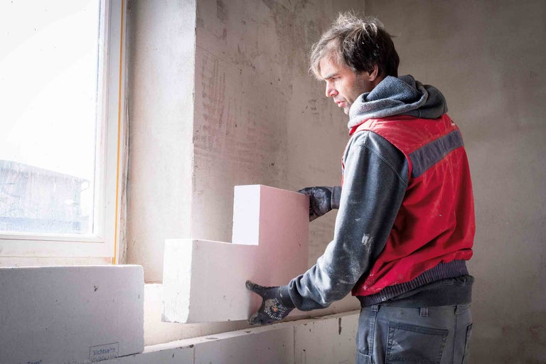 Un bărbat montează blocuri de beton celular la construirea unei case.