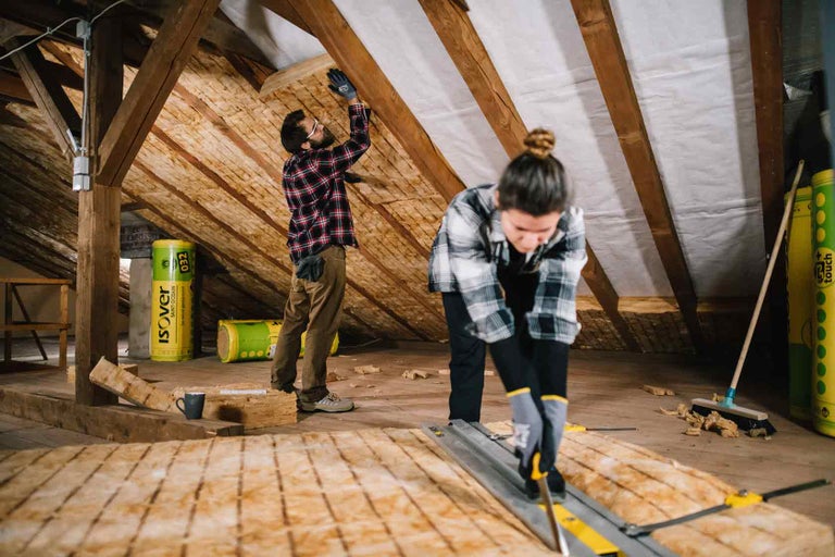 Izolație mansardă cu două persoane care instalează și taie material izolator