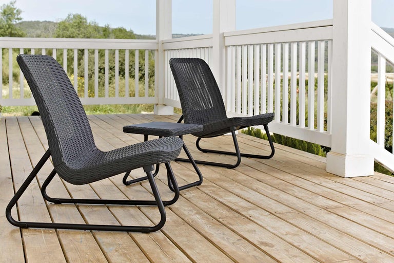 Două scaune din ratan și o masă pe o terasă din lemn.