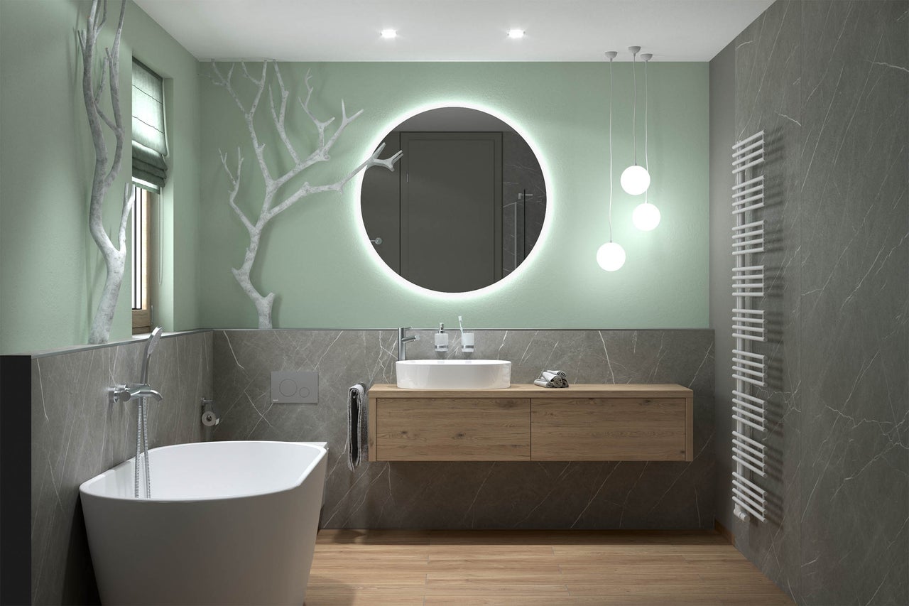 Baie modernă cu cadă de sine stătătoare, dulap de lavoar din lemn, oglindă rotundă cu LED și plăci ceramice mari cu aspect de marmură.
