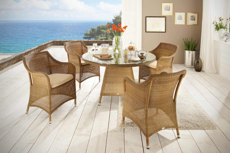 Set de mobilier de grădină cu scaune din ratan și masă rotundă cu blat de sticlă pe o terasă cu vedere la mare