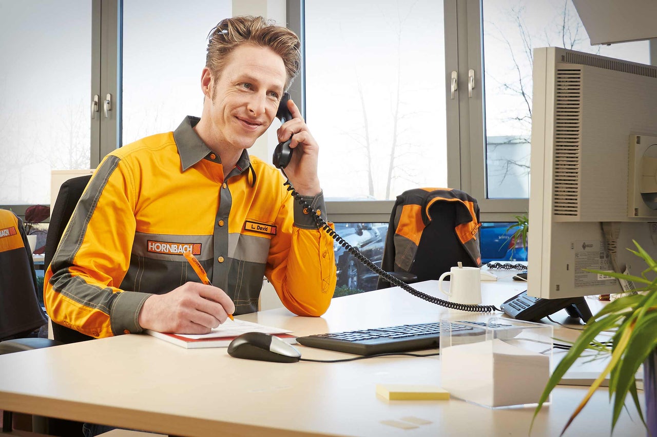Un angajat Hornbach vorbește la telefon și ia notițe la biroul său.