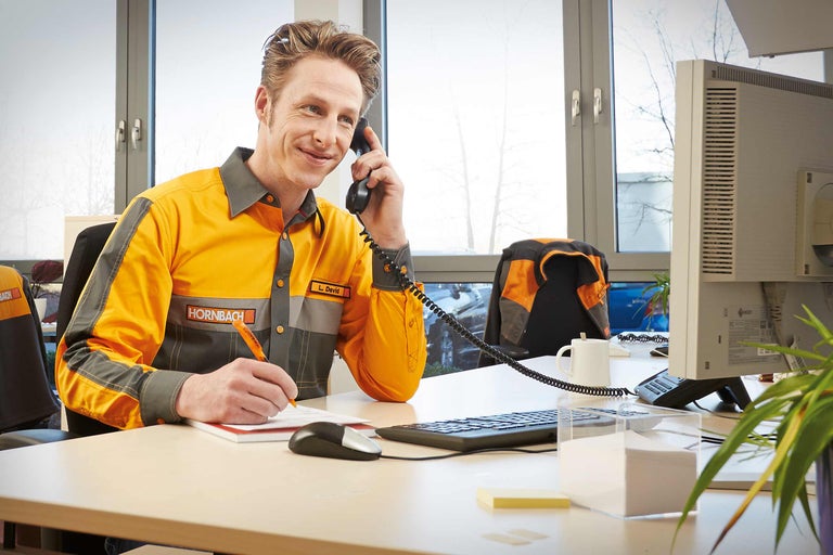 Un angajat Hornbach vorbește la telefon și ia notițe la biroul său.
