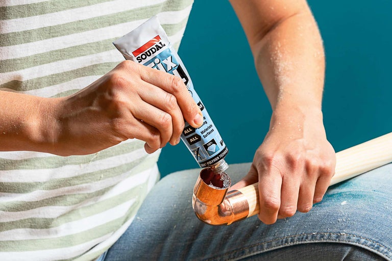 O persoană aplică adeziv dintr-un tub Soudal Fix All pe o țeavă de cupru