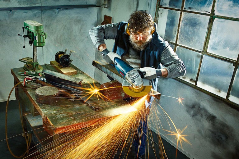 Un bărbat lucrează cu un polizor unghiular într-un atelier și sar scântei.