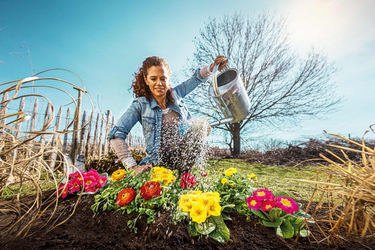 Femeie udând flori cu o stropitoare în grădină.