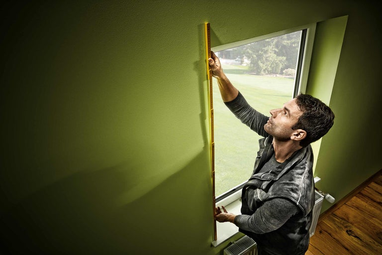Bărbat măsoară rama ferestrei cu un metru pliant