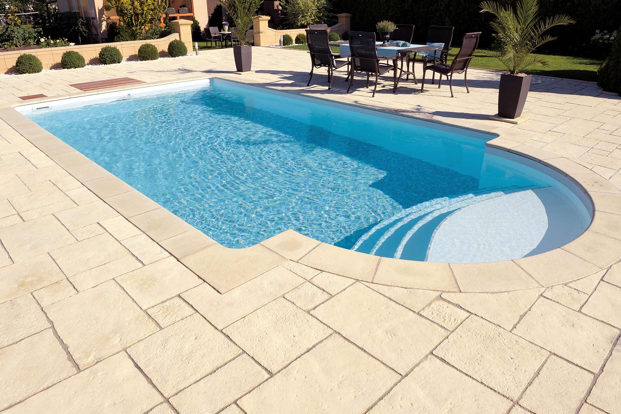Piscină cu plăci de piatră deschise la culoare și zonă de relaxare în grădină