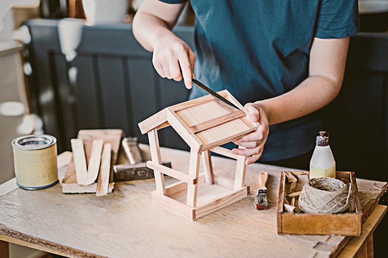 O persoană pilește o căsuță pentru păsări din lemn pe o masă cu unelte.
