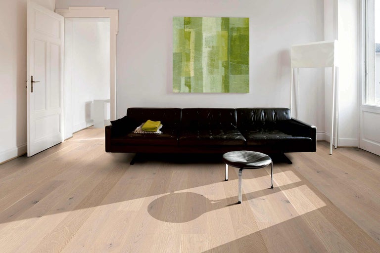 Pardoseală deschisă la culoare, din lemn, într-un living cu canapea și operă de artă