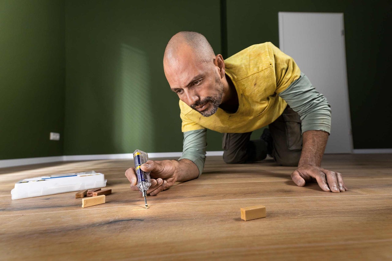 Bărbat reparând parchet laminat cu instrument de reparare și ceară