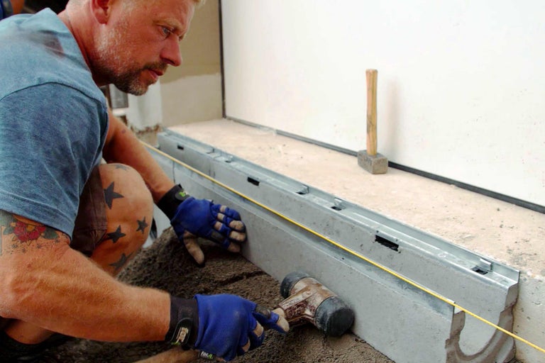 Bărbat așază canal de drenaj cu ciocanul pe pietriș