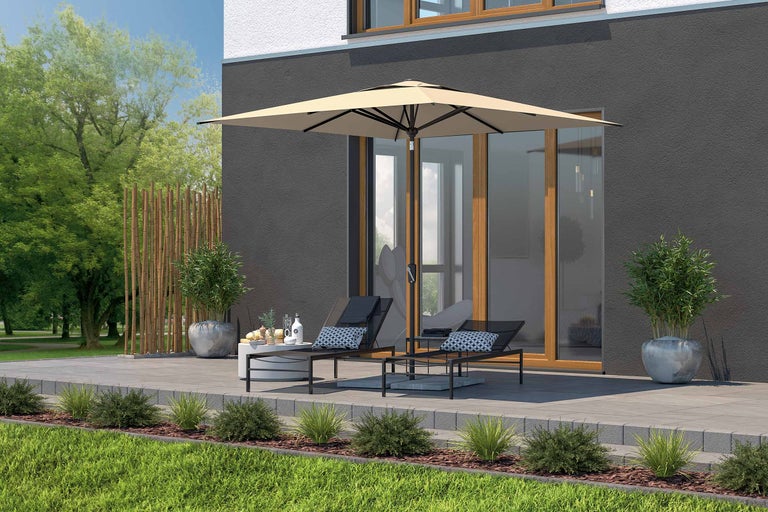 Terasă cu umbrelă de soare, șezlonguri și măsuță laterală în fața unei case