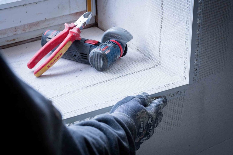 Instalator fixează țesătura de armare, în fundal clește lateral și polizor unghiular