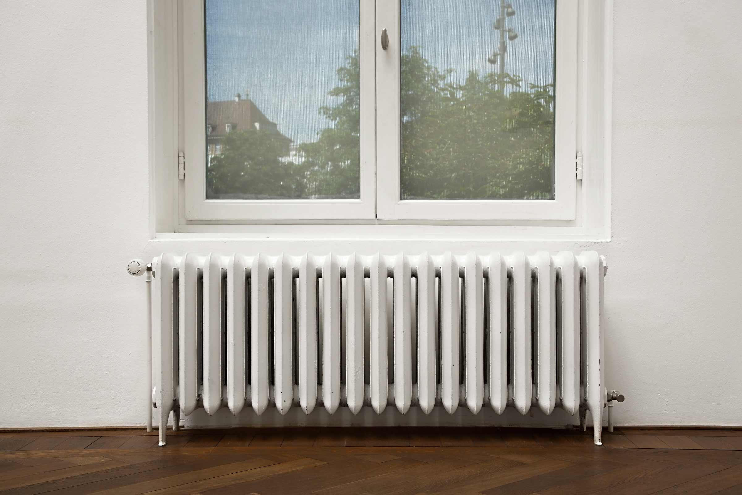 Radiator alb sub o fereastră pe o podea de lemn